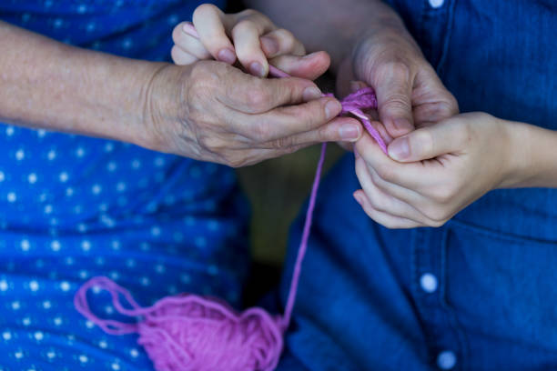 Grandmother teaches her granddaughter to crochet. Hands of elderly woman and young girl. Concept of harmony relationship between generations. stock photo