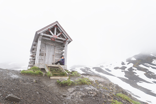 Young ethnic woman relaxes for a short while on the front porch of a cabin while she hikes up an Alaskan glacier.