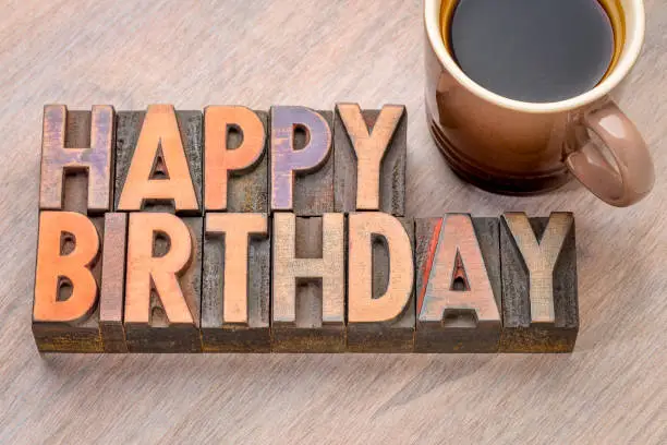 Happy Birthday greeting card in vintage letterpress wood type against grained wood with a cup of coffee