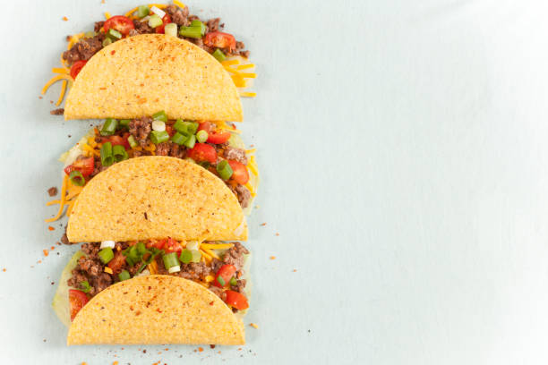 Mexican food crunchy beef tacos in a row. Mexican food!  Delicious crunchy beef tacos lined up in a row.  The tacos include ground beef, cheese, tomatoes and onions.  Copyspace at side. tacos stock pictures, royalty-free photos & images