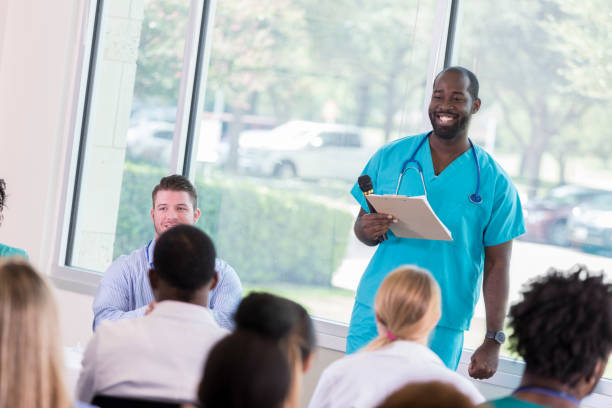 profissional de saúde masculina fala ao público dos prestadores de cuidados de saúde - male black medical student mature student - fotografias e filmes do acervo