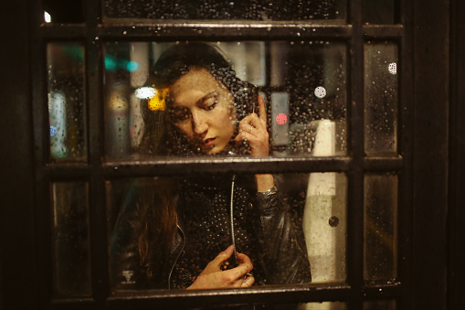 Young woman talking on the public payphone in London at night.