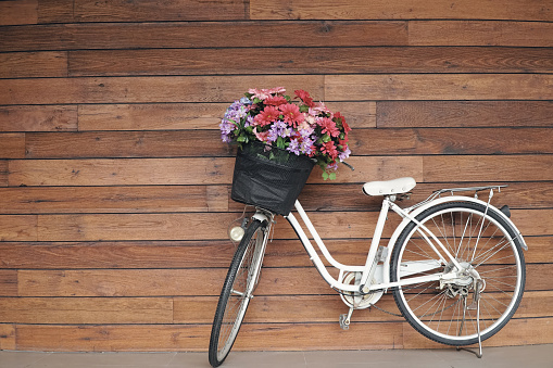 White bicycle Have a basket with a bouquet of flowers. The park next to the wooden wall in vintage. copy space.