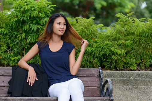 Portrait of young beautiful Asian woman relaxing at the park in Bangkok Thailand vertical shot