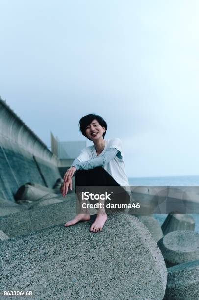 Smiling Woman Sitting On Tetrapod At Beach Stock Photo - Download Image Now - 30-39 Years, Adult, Adults Only