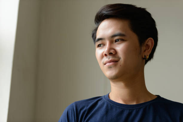 istock Young Asian man wearing blue shirt inside room looking out through the window 863310028
