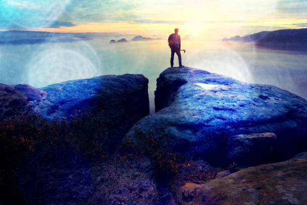 istock Sharp rear man silhouette on rocky peak. Satisfy hiker enjoy view. Tall man on rocky cliff watching down to landscape. 863371048
