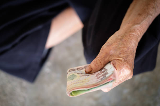 istock Hand the old man the banknote thai money for saving. money saving concept, benefits elderly people, graybeard holding and  showing money in hand , Local Thailand 863371302