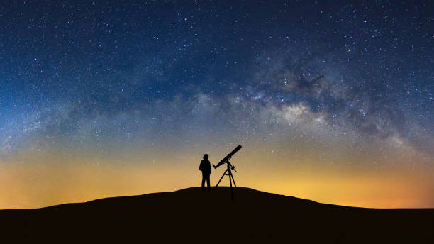 istock Silhouette of a standing man with telescope watching the wilky way galaxy 863376038