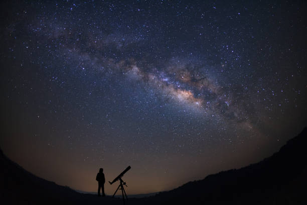 istock Silhouette of a standing man with telescope watching the wilky way galaxy 863377876