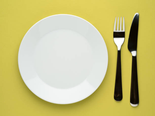 istock Blank flat plate, knife, fork on a color yellow table, top view. 863451174