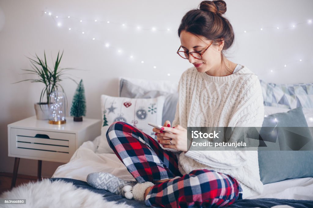 Lazy morning in bed Young women sitting on bed and using mobile phone Christmas Stock Photo