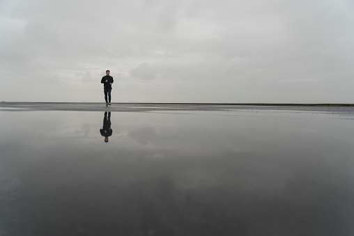 photo of male athlete running through puddle against cloudy sky,with relfection in puddle.