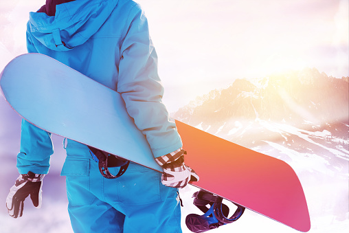 Ski concept with close up photo of snowboarder with snowboard in hands standing on background of big mountain