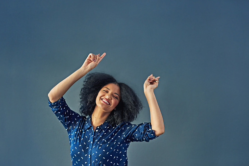 Studio shot of a happy young woman dancing against a gray background