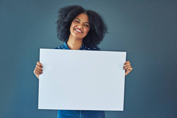 Now here's something that'll make you smile Studio shot of a young woman holding up a blank placard against a gray background placard photos stock pictures, royalty-free photos & images