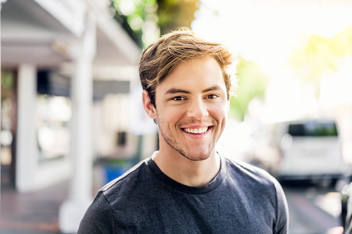 Close-up portrait of young man. Smiling handsome male is wearing casuals. He is in city on sunny day.