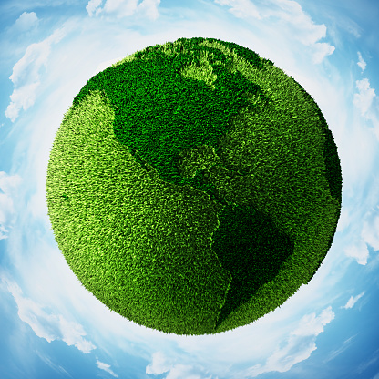 Grass covered globe with world map surrounded with blue sky showing Americas.