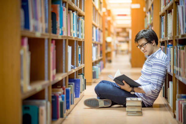 istock Young Asian man university student reading book in library 863492390