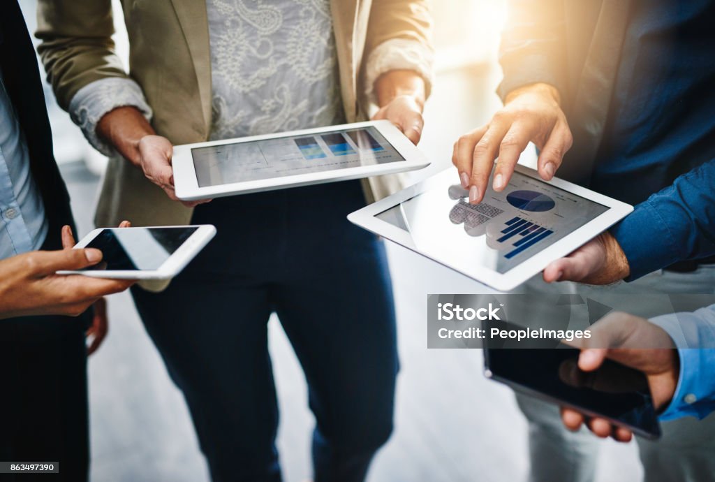 I'll share the information with you... Cropped shot of unrecognizable businesspeople using their wireless devices in the office Technology Stock Photo