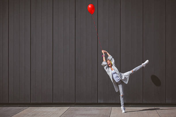 Young woman dancing and holding red balloon against the grey wall stock photo