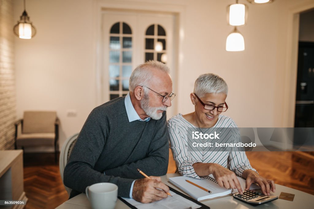 We might just be able to afford that vacation! A happy senior couple calculating their finances in a beautiful home. Retirement Stock Photo