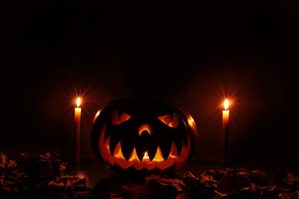 a terrible Halloween pumpkin glowing in the dark amid the wilted leaves and light from the candle