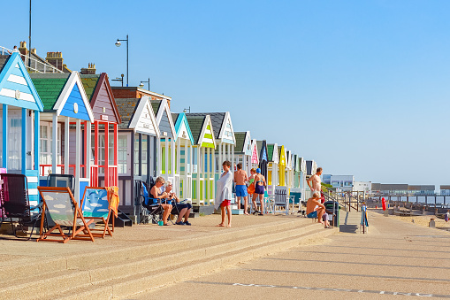 Southwold, UK - September 11, 2017 - People enjoying the sunshine on the promenade of Southwold beach lined with a row of beach huts