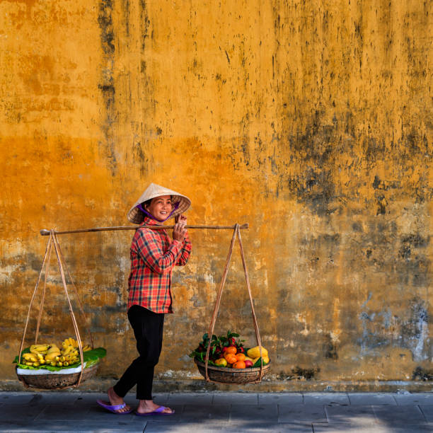 Vietnamese woman selling tropical fruits, old town in Hoi An city, Vietnam Vietnamese woman selling tropical fruits, old town in Hoi An city, Vietnam. Hoi An is situated on the east coast of Vietnam. Its old town is a UNESCO World Heritage Site because of its historical buildings. vietnam stock pictures, royalty-free photos & images