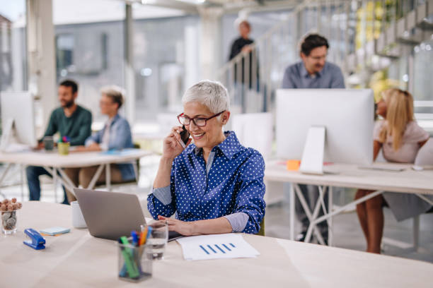 istock Happy mature freelancer talking on smart phone while working on laptop in the office. 863559044
