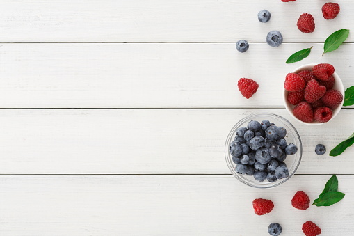 Assorted garden and wild berries background. Mix of fresh organic strawberries, raspberries, blueberries and blackberries in glass bowl on white wooden table, top view, copy space