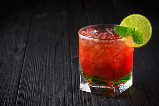 Red alcohol cocktail with mint and lime on black wooden background