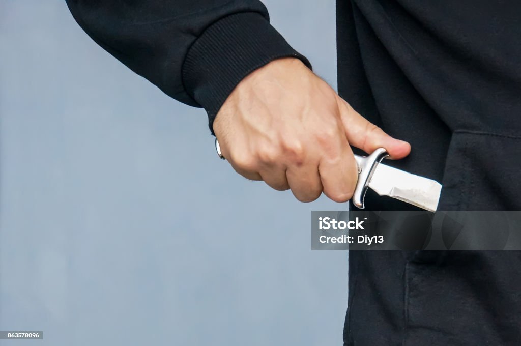 Hand from the pocket of the black jacket pulls out a folding knife close up. Hand from the pocket of the black jacket pulls out a folding knife close up. Extortion and intimidation. The concept of a crime of violence. mafia. Hiding Stock Photo