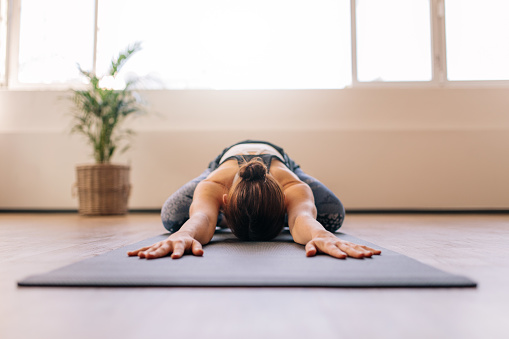 Fit woman performing child yoga pose at gym class. Fitness woman working out on yoga mat indoors.