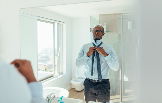 Businessman wearing a tie looking at the mirror. Man dressing up looking at the mirror in bathroom.