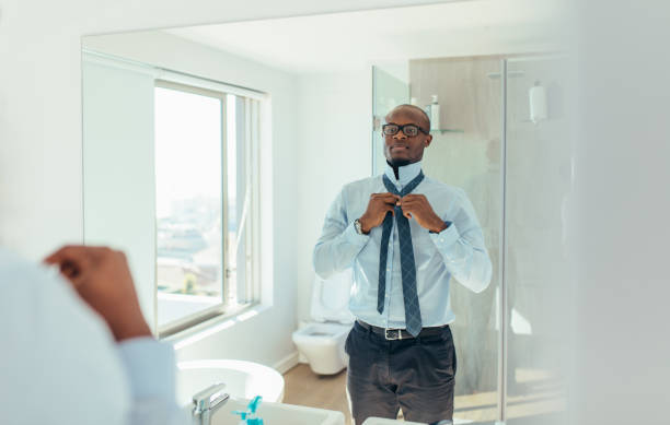 Man getting ready for office Businessman wearing a tie looking at the mirror. Man dressing up looking at the mirror in bathroom. getting dressed stock pictures, royalty-free photos & images