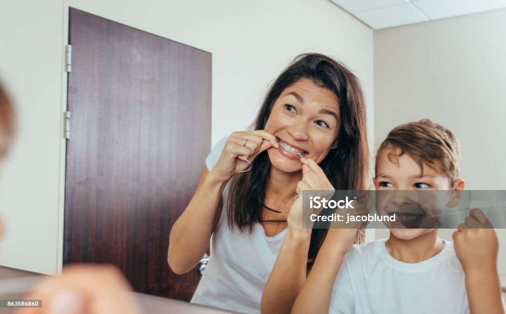 Mother and son cleaning teeth with dental floss Little boy with his mother in bathroom cleaning teeth with dental floss. Woman with son looking in mirror and cleaning teeth. Dental Floss Stock Photo