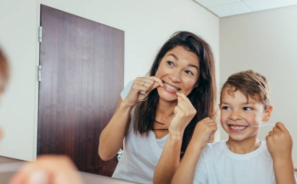 Mother and son cleaning teeth with dental floss Little boy with his mother in bathroom cleaning teeth with dental floss. Woman with son looking in mirror and cleaning teeth. dental floss stock pictures, royalty-free photos & images