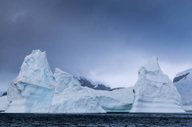 огромный айсберг, установленный на фоне темных облаков - glacier antarctica crevasse ice стоковые фото и изображения