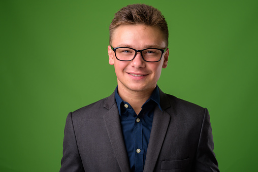 Studio shot of young handsome businessman wearing eyeglasses against green background horizontal shot