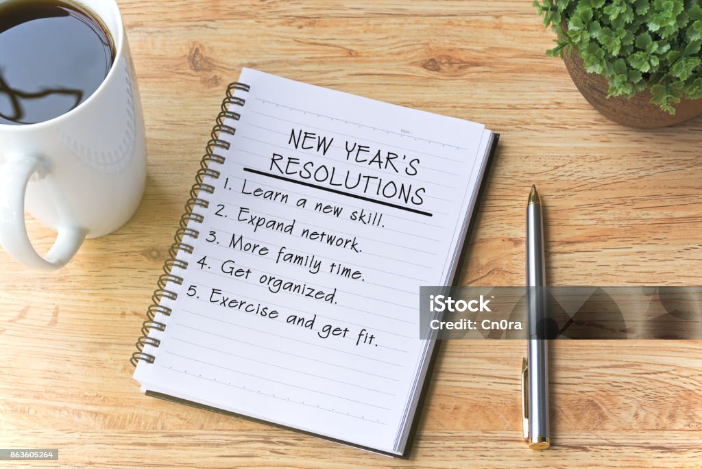 Resoluciones de año nuevo escritas en el Bloc de notas con pluma, café y planta en mesa de madera. - Foto de stock de Propósito de año nuevo libre de derechos