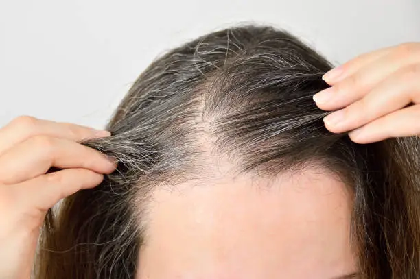 woman is checking white hair while looking at the mirror