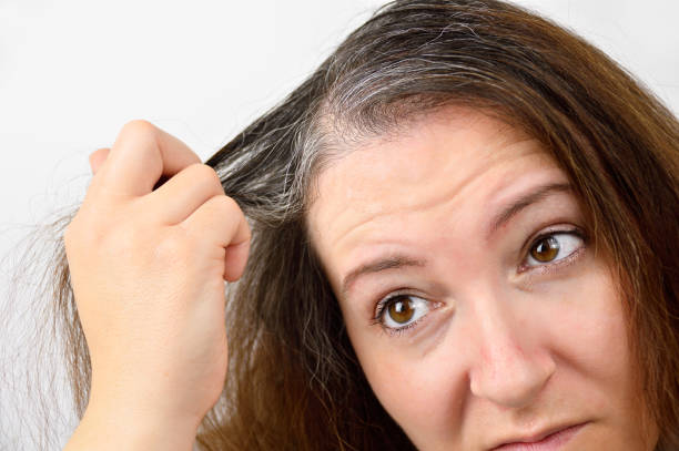 Young woman shows her gray hair woman is checking white hair while looking at the mirror hair care women mature adult human skin stock pictures, royalty-free photos & images