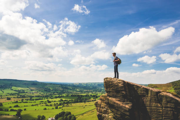 Teenage Boy Stands at Edge in Peak District A teenage boy stands at the edge of a rocky outcropping while rambling along The Roaches in Peak District National Park, United Kingdom. He looks over the rolling green countryside of Staffordshire on a warm summer day. peak district national park photos stock pictures, royalty-free photos & images