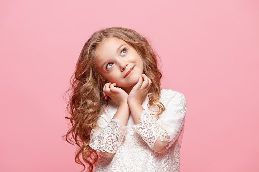 The beautiful little girl in long dress standing and posing over pink background