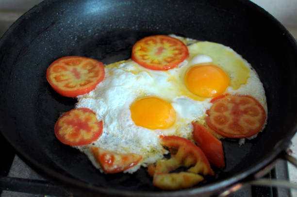 istock Two fried eggs in black frying pan and slices tomato. Process of cooking 863705546