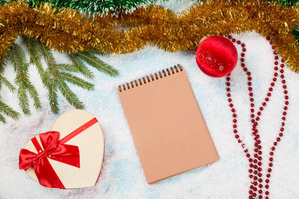 istock Christmas fir tree branches on wooden board with blank notebook with spangle, christmas ball and giftbox on snow. Christmas or new year frame for your project with copy space on the blank notebook. 863728374