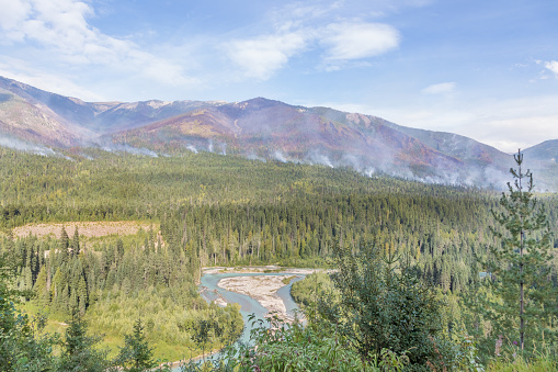 View from the trans Canada highway on the valley and and mountains with wildfire in a distance. Burn scars can be seen in the forest.