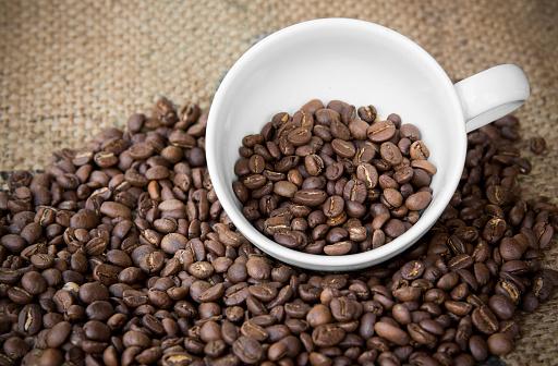 arabica coffee beans in coffee cup with sack cloth background.roasted coffee beans pattern