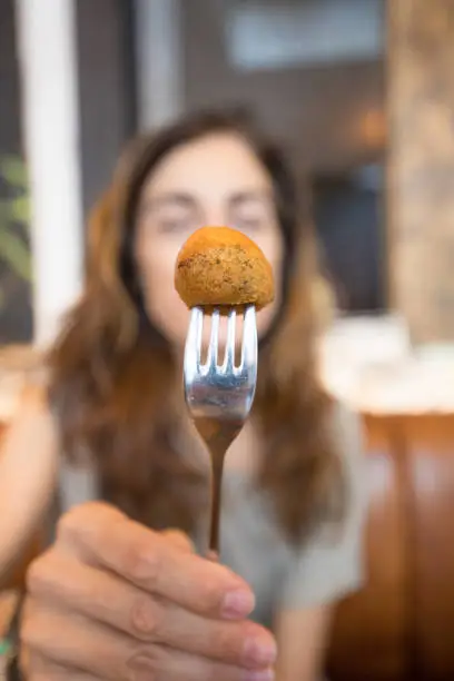 close up of fried codfish fritter, woman is showing it holding in fork at restaurant